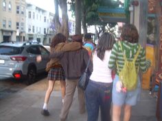 three people walking down the sidewalk in front of parked cars