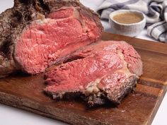 two pieces of meat sitting on top of a wooden cutting board next to a cup of sauce