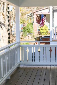 an american flag is hanging on the back porch of a house with white railing and wood flooring