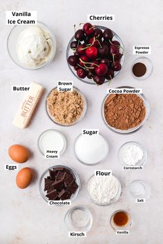 the ingredients to make an ice cream dessert laid out on a white counter top, including cherries and chocolate