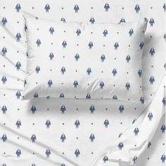 a bed with white sheets and blue robot print on the pillowcase, along with two pillows