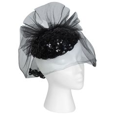 A knockout accessory for New Years Eve or a black tie event, this cocktail hat is as petite as a fascinator but packs the punch of a wide brim. Both glitzy and understated, it balances a glittering sequin skull cap with an alluring cage veil for an unforgettably sophisticated look. Rigid oval calot cap with pavé black sequins; attached tulle birdcage veil with rear center self bow and tails trimmed with sequins. Fully lined in black acetate. material: acetate, tulle veiling, sequins noteworthy: Cossack Hat, Cage Veil, Historical Hats, Black Straw Hat, Veiled Hats, Velvet Hat, Birdcage Veil, Mom Hats, Feather Hat