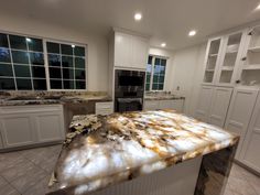 a large kitchen with marble counter tops and white cabinetry, along with an island in the middle