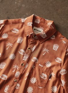 The Take It Greasy is a fun cut-n-sew button-up shirt. It is made of soft, high quality cotton blend fabric and has tortoise buttons. The rust colored casual shirt features a bold all-over print of cheeseburgers, fries, palm trees, and the sun. Stay sophisticated while not-so-subtly letting everyone know you're all about paradise and a good burger. Features: Comfy & Lightweight 55% Cotton 45% Rayon Blend. Rust. Unique All-Over Print Design. Vacation Shirt Collar, Tortoise Buttons. Available in M Casual Brown Shirt With Graphic Print, Brown Cotton Printed Tops, Brown Graphic Print Button-up Top, Printed Brown Shirt For Fall, Cotton Button-up Camp Shirt With All Over Print, Printed Brown Button-up Shirt, Casual Brown Camp Shirt With Button Closure, Brown Printed Button-up Shirt, Orange Cotton Shirt With Print