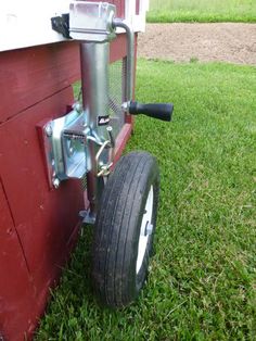 a wheel attached to the side of a red building with grass in front of it