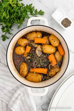 a pot filled with stew and carrots next to some parsley on the side