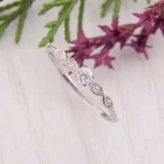 a diamond ring sitting on top of a wooden table next to purple flowers and greenery