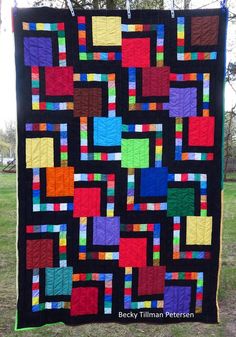 a colorful quilt hanging on a clothes line in the grass with trees in the background