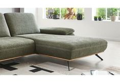 a green sectional couch sitting on top of a white rug in a living room next to a window