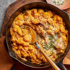 a skillet filled with pasta and meat covered in parmesan cheese on a wooden cutting board