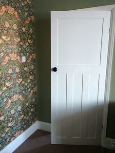 an empty room with a white door and wallpaper on the walls, next to a carpeted floor