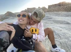 a man and woman sitting on top of a rock next to each other with sunglasses on