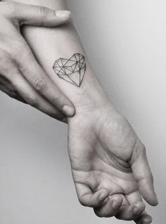 two hands holding each other with a small diamond tattoo on the wrist and heart in the middle