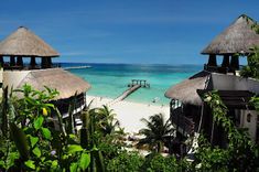 the beach is surrounded by palm trees and thatched huts, with blue water in the background