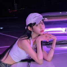 a woman sitting on the hood of a car in front of a purple lit background