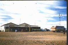 an old car is parked in front of a building on the side of a dirt road