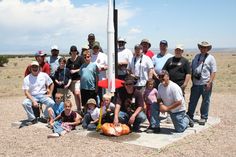 a group of people posing for a photo in front of a flag pole with an arrow on it