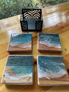 four square coasters sitting on top of a wooden table next to a candle holder