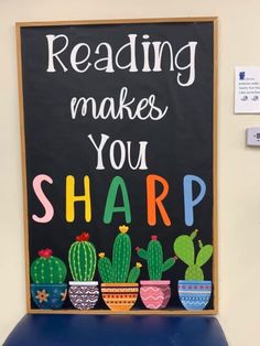 a chalkboard with the words reading makes you sharp written in front of potted cacti