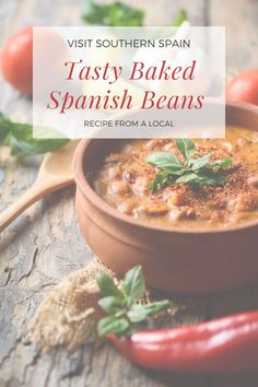 a brown bowl filled with baked spanish beans next to red peppers and basil on a wooden table