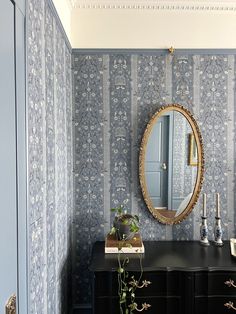 a black dresser and mirror in a room with blue wallpaper on the walls, along with a potted plant