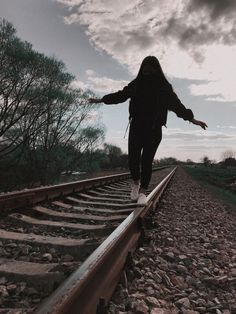 a woman is walking on the train tracks with her arms outstretched in front of her