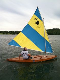 a man sitting in a small sailboat on the water with a blue and yellow sail