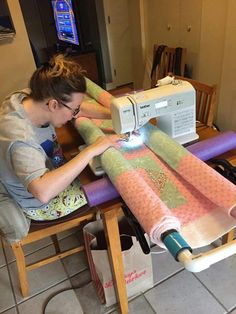 a woman sitting at a table using a sewing machine to sew on some fabric