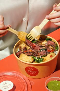 a person holding a wooden fork over a bowl of food