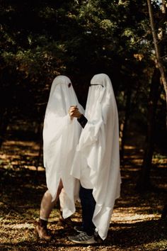 two people dressed in white are walking through the woods with their heads covering each other