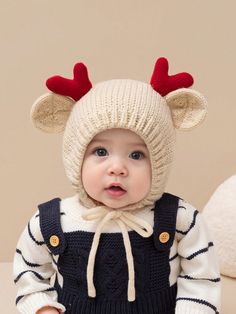 a baby wearing a knitted reindeer hat and overalls with red antlers on it's ears