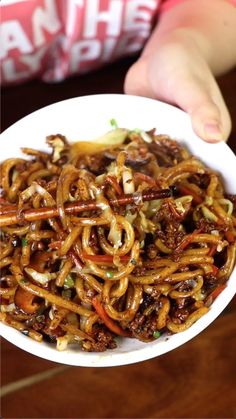 a person holding a white bowl filled with noodles