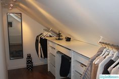 an attic bedroom with clothes hanging on the rails and closet space in front of it