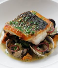 a white plate topped with fish and clams on top of sauced broth