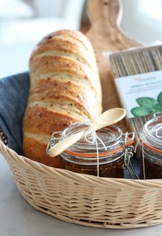 bread and jams in glass jars sitting on a basket next to a wooden spoon