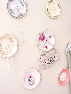 there are many plates on the wall with flowers and purses hanging from it's sides