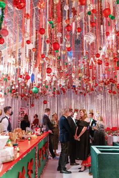 people standing in front of a long table covered with christmas decorations and ornaments hanging from the ceiling