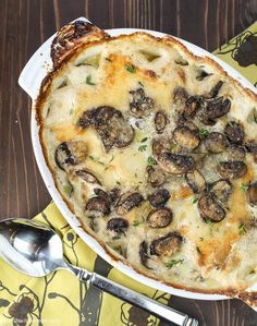 a casserole dish with cheese and mushrooms in it on a yellow napkin next to silverware