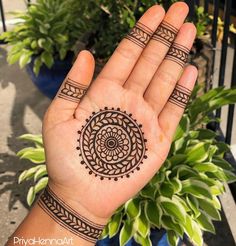 a person's hand with a henna tattoo on it and some plants in the background