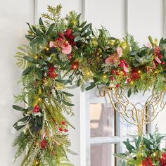 two christmas wreaths hanging from the side of a white building with lights on them