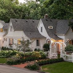 a white house surrounded by lush green trees and flowers in the front yard at night