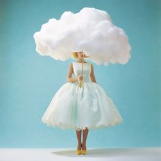 a woman in a white dress is standing under a cloud with a yellow umbrella on her head