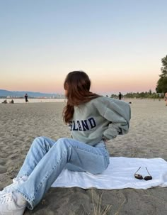 a woman sitting on top of a white blanket next to a pair of sunglasses at the beach