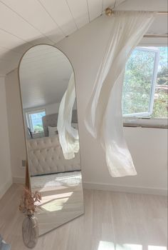 a large mirror sitting in the middle of a room next to a window with sheer curtains