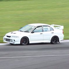 a white car driving down a race track in front of a green grass covered field