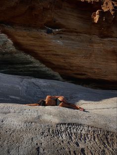 a woman laying on top of a sandy beach next to a cliff and water hole