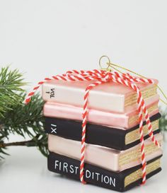 a stack of books ornament sitting on top of a christmas tree next to a pine branch