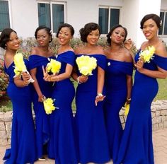 a group of women standing next to each other wearing blue dresses and holding yellow flowers