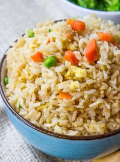 a blue bowl filled with rice and veggies next to broccoli on a table