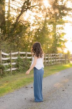 a woman is walking down the road with her back to the camera and she's wearing blue pants